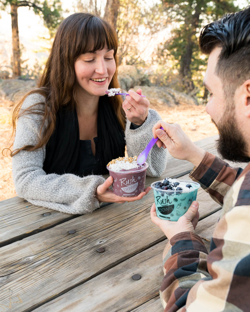 A couple of millenials outside enjoying two Rush Bowls smoothie bowls.